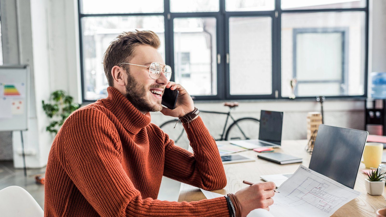 Unternehmer im Gespräch am Telefon, mit Plan und Stift am Schreibtisch