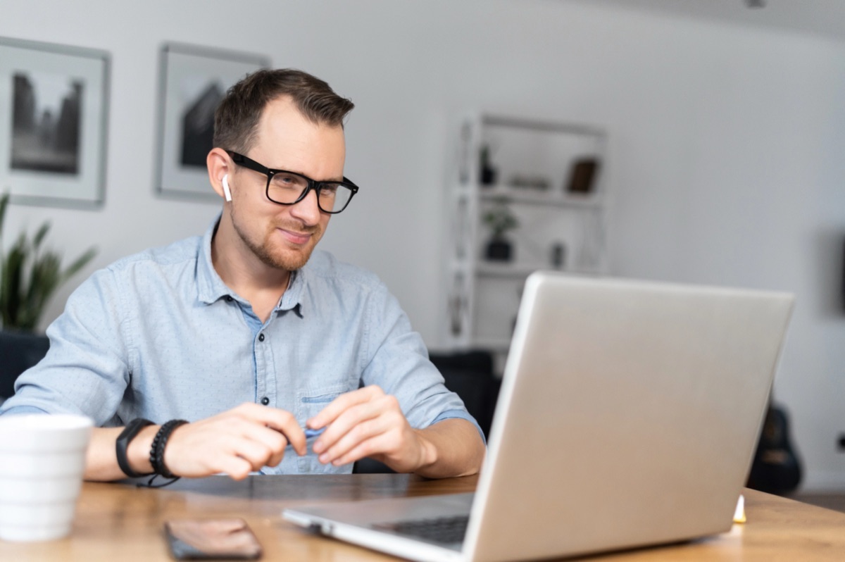 Mann mit Brille sitzt entspannt lächelnd vor seinem Laptop in einem Online-Gespräch